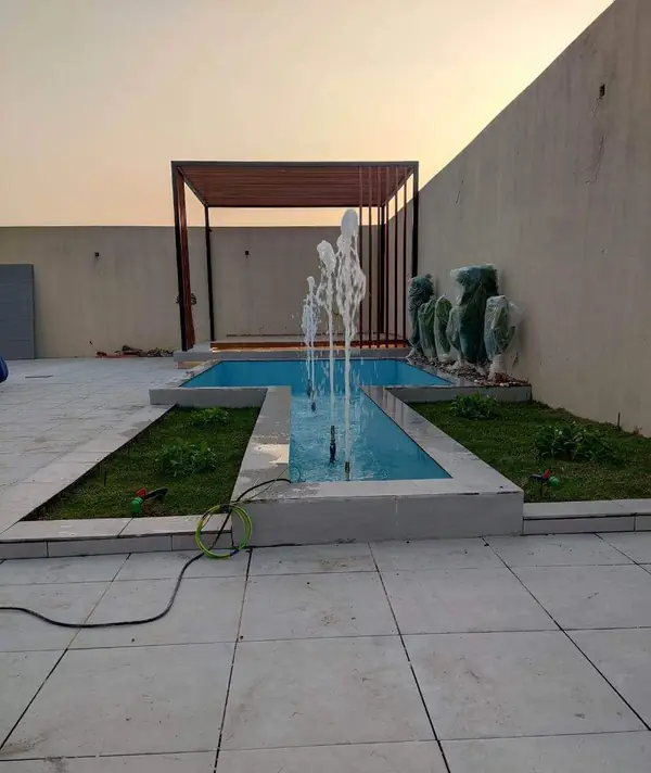 قناة مائية بنوافير عمودية وسط ممشى بلاطي وعشب — تنفيذ غصون الصفوة